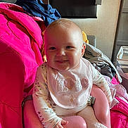 Gracelynn is registered to the contest to win money with this photo: baby, child, smile, pink_baby_seat, bib, floral_pajamas, indoor, blanket, clothing, pile, face, person, cute, infant, seated, cheerful, happy, soft_lighting, home, cozy