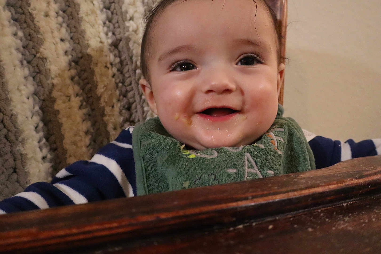 Liam is registered to the contest to win money with this photo: baby, infant, child, smile, bib, food, messy, cheeks, eyes, closeup, portrait, highchair, wooden_tray, blanket, striped_sleeve, indoor, adorable, drool, eyelashes, happy
