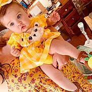 Gracie is registered to the contest to win money with this photo: baby, child, yellow_dress, bow, bear_applique, sandal, lemon, floral_dress, adult, indoor, furniture, desk, baby_gear, person, cute, holding, blue_eyes, hair, skin, footwear