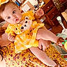 baby, child, yellow_dress, bow, bear_applique, sandal, lemon, floral_dress, adult, indoor, furniture, desk, baby_gear, person, cute, holding, blue_eyes, hair, skin, footwear