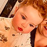 Gracie is registered to the contest to win money with this photo: toddler, child, curly_hair, rosy_cheeks, blue_eyes, cream_outfit, blueberry_print, zipper, indoor, adult, smile, face, person, closeup, young_child, human, skin, portrait, warm_lighting, cozy