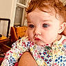 baby, child, infant, face, hair, eyes, expression, clothing, onesie, floral_pattern, arm, skin, indoor, window, couch, furniture, person, holding, curious, closeup