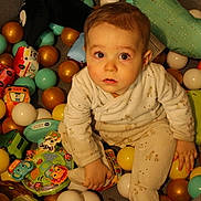 Raphaël a rejoint le concours — aidez-le/la à gagner de superbes lots ! baby, child, toddler, ball_pit, toys, plastic_balls, pajamas, sitting, looking_up, curious, indoor, playtime, closeup, portrait, cute, giraffe_toy, colorful, expression, soft_toys, floor