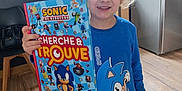 Abel a rejoint le concours — aidez-le/la à gagner de superbes lots ! blond_hair, blue_shirt, book, boy, cartoon_character, child, furniture, happy, holding, home_interior, kitchen, person, portrait, refrigerator, shelf, smiling, sonic_book, standing, window, wooden_floor