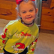Ariel is registered to the contest to win money with this photo: child, girl, red_bow, green_sweater, black_pants, black_boots, smiling, indoor, wooden_wall, window, playful_pose, happy, cute, fashion, choker, long_hair, light, floor, holiday_theme, portrait