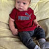 baby, child, puma, tshirt, red_clothing, gray_pants, socks, sitting, couch, furniture, indoors, person, face, expression, serious, young_child, skin, hair, comfort, casual_clothing