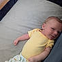 baby, infant, yellow_onesie, dinosaur_pants, playpen, soft_surface, sleepwear, child, newborn, cute, resting, indoor, portrait, small_hands, relaxed, face, skin, head, lying_down, clothing