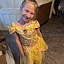 child, girl, princess_dress, yellow_dress, smile, indoor, tile_floor, playful, happy, dress_up, costume, footwear, flip_flops, long_hair, brown_hair, background, door, wall, paper_bags, room