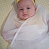baby, infant, yellow_headband, bow, white_sheer_fabric, blanket, quilted_blanket, closeup, portrait, face, blue_eyes, wrapped, lying_down, soft_texture, cute, child, newborn, peaceful, indoors, person