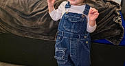 Gabriel joined the competition — help win amazing prizes! bed, blanket, casual_clothing, child, cute, denim_overalls, earrings, flooring, happy, home, indoor, laughing, natural_light, person, smiling, sneakers, standing, toddler, window, young
