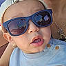 toddler, child, sunglasses, cap, face, mouth, earring, clothing, person, adult, necklaces, jewelry, casual, portrait, closeup, blue_sweater, hat, fashion, sunlight, outdoor