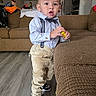 bow_tie, boy, casual, child, clothing, couch, curious, expression, floor, furniture, home, indoor, living_room, person, portrait, sneakers, standing, suspenders, toddler, toy