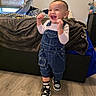 Gabriel joined the competition — help win amazing prizes! child, toddler, smiling, standing, denim_overalls, white_shirt, sneakers, indoor, bed, blanket, window, flooring, happy, person, casual_clothing, earrings, home, furniture, curtains, joy