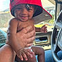Amari is registered to the contest to win money with this photo: adult_hand, automobile, baby, car_interior, child, closeup, cute, daylight, diaper, fingernails, foot, hat, person, playful, red_cap, seatbelt, seated, skin, smiling, window