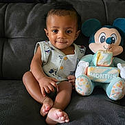 Amari joined the competition — help win amazing prizes! baby, child, infant, plush_toy, mickey_mouse, block, months, couch, sofa, clothing, smile, face, sitting, indoor, toy, cute, comfort, furniture, person, portrait