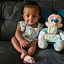 baby, child, infant, plush_toy, mickey_mouse, block, months, couch, sofa, clothing, smile, face, sitting, indoor, toy, cute, comfort, furniture, person, portrait