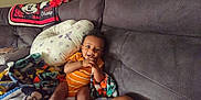 Amari is registered to the contest to win money with this photo: baby, child, couch, blanket, pillow, pacifier, beads, orange_onesie, mickey_mouse, smiling, indoor, happy, seated, curly_hair, furniture, cute, playful, comfort, home, person