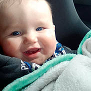 James is registered to the contest to win money with this photo: baby, smiling, blanket, blue_eyes, car_seat, child, face, happy, cute, infant, cozy, cheeks, portrait, clothing, soft, indoor, warm, comfort, toddler, seat