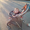 baby, casual, child, clothing, curious, daylight, expression, footwear, infant, outdoor, parked, pavement, person, seat, shadow, stroller, summer, sunlight, transport, wheel