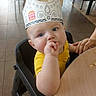 baby, burger_king, chair, child, curious, cute, dining, floor, hand, high_chair, indoor, infant, paper_crown, person, portrait, restaurant, seat, table, thumb_sucking, yellow_shirt
