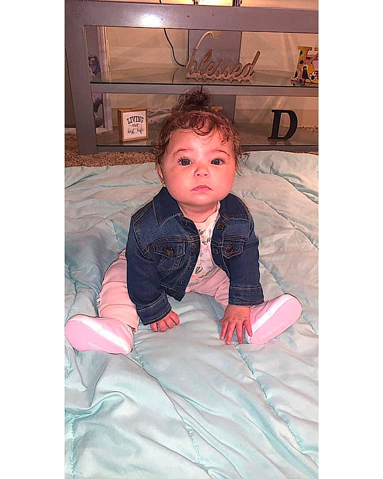 Kamarii is registered to the contest to win money with this photo: baby, cheek, child, face, finger, head, outerwear, person, pink, sitting, toddler, vacation