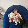 baby, child, stuffed_toy, plush, blue_chair, indoor, smiling, cute, person, toy_dog, mickey_mouse, floor, white_wall, clothing, sitting, happy, soft_toy, homedecor, bag, cozy