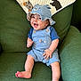 baby, child, smiling, hat, blue_clothing, overalls, green_chair, quilt, dog_pattern, cute, happy, indoor, infant, sitting, portrait, clothing, foot, hand, face, cozy
