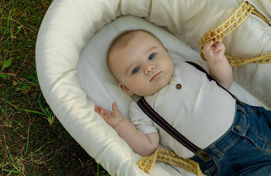 Jameson is registered to the contest to win money with this photo: baby, infant, basket, clothing, denim, suspenders, white_shirt, blue_eyes, grass, outdoor, cute, portrait, child, face, head, soft_light, nature, relaxing, lying_down, skin