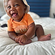 Kamari joined the competition — help win amazing prizes! baby, infant, child, smiling, laughing, orange_shirt, hat, bed, white_bedspread, cute, happy, indoors, portrait, skin, hand, foot, person, headwear, playful, young