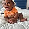 baby, infant, child, smiling, laughing, orange_shirt, hat, bed, white_bedspread, cute, happy, indoors, portrait, skin, hand, foot, person, headwear, playful, young