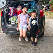Brent'Lee joined the competition — help win amazing prizes! children, kids, car_trunk, backpack, bags, smiling, outdoor, casual_clothes, playful, sibling, holding_hands, daytime, concrete, residential_area, greenery, summer_clothes, footwear, happy, family, transportation