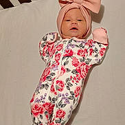 Meredith is registered to the contest to win money with this photo: baby, infant, onesie, floral_pattern, pink_bow, hat, sleeping_area, crib, soft_surface, cute, child, newborn, clothing, portrait, resting, indoors, face, headwear, baby_gloves, footed_pajamas