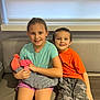 child, children, baby, newborn, sibling, couch, indoor, smile, happy, holding, striped_blanket, orange_shirt, camouflage_pants, headband, shorts, portrait, family, together, seated, casual_clothing