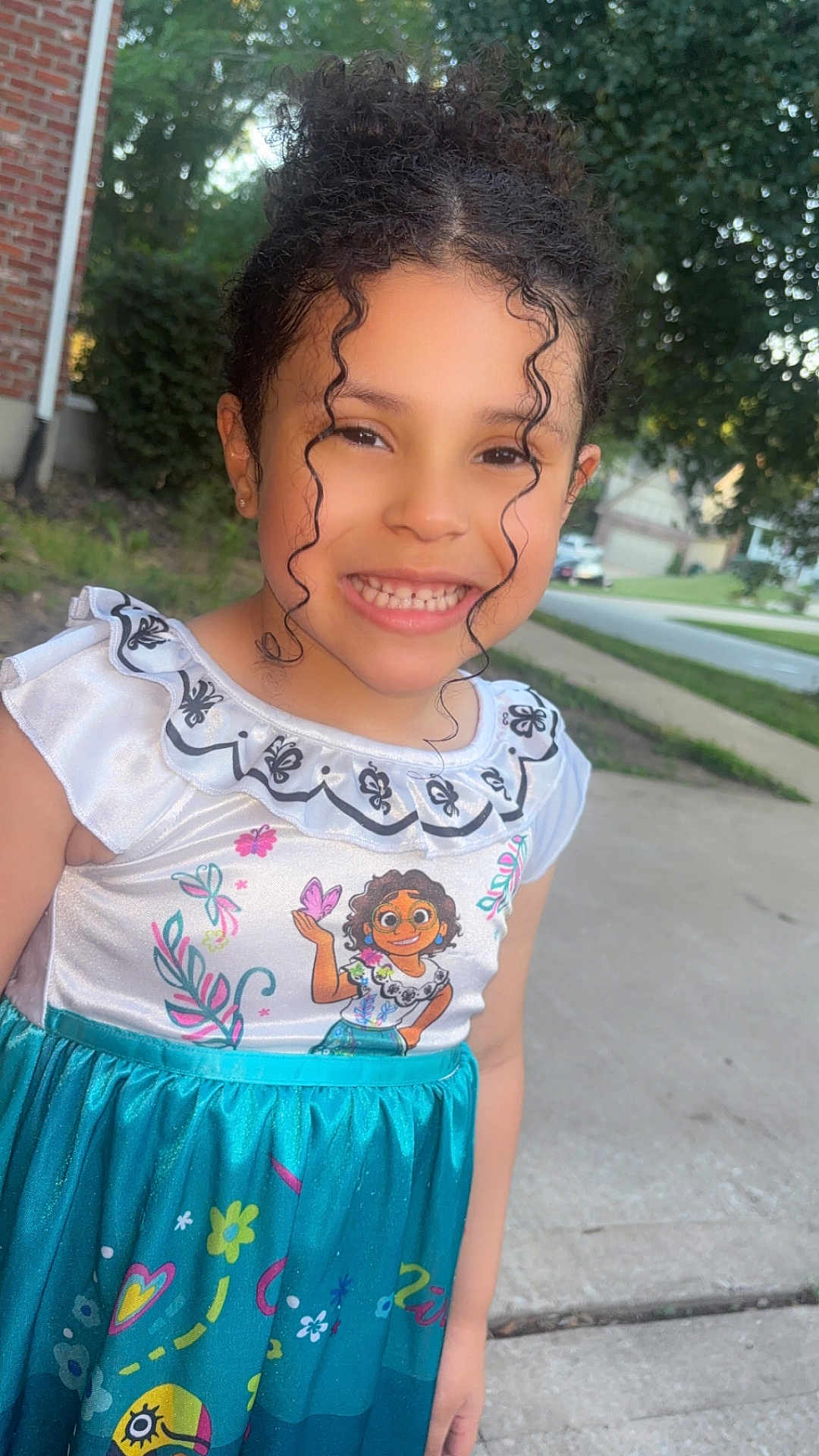 Aria is registered to the contest to win money with this photo: child, girl, smile, curly_hair, dress, outdoor, suburb, sidewalk, cartoon_character, happy, young, portrait, colorful_clothing, nature, greenery, daylight, casual, cute, person, playful