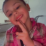 Aria is registered to the contest to win money with this photo: child, smiling, indoor, plaid_jacket, peace_sign, person, young, portrait, face, earrings, window, carpet, door, furniture, casual_clothing, happy, gesture, curly_hair, cozy, home