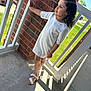 Aria is registered to the contest to win money with this photo: child, girl, white_dress, curly_hair, sandals, brick_wall, porch, outdoor, daylight, shadow, concrete_floor, hair_bun, side_view, casual_pose, summer, green_grass, railings, thoughtful, young, fashion