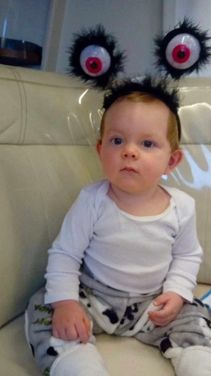 Kayston participe au concours pour gagner de l'argent avec cette photo : toddler, child, baby, headband, eyeballs, fuzzy, couch, white_shirt, patterned_pants, indoor, sitting, curious, serious, leather_couch, hand, footwear, person, cute, costume, funny_accessory