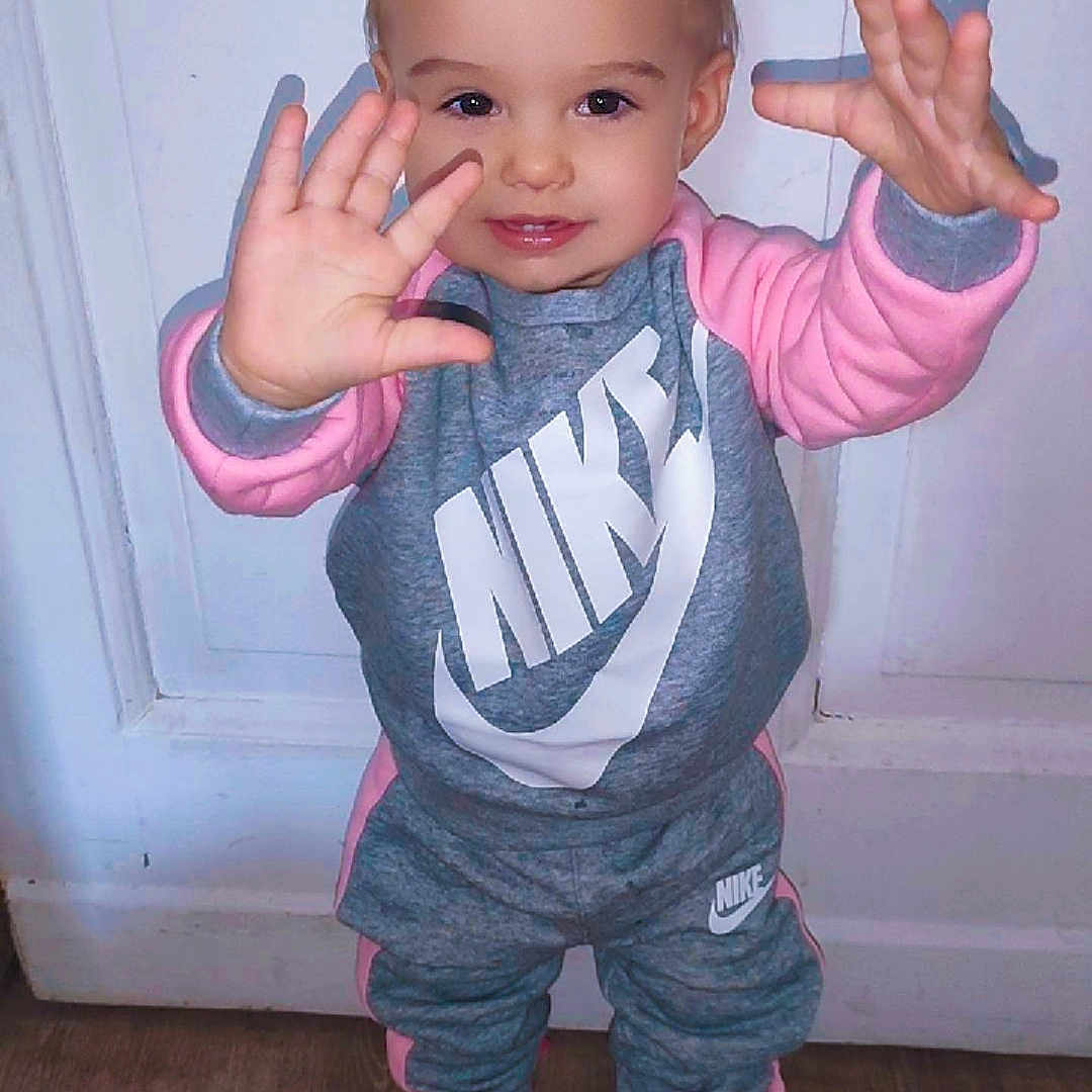Jade a rejoint le concours — aidez-le/la à gagner de superbes lots ! casual_clothing, child, cute, fashion, full_body, hands_up, happy, indoor, nike, playful, portrait, smiling, sneakers, sporty, standing, toddler, tracksuit, white_door, wooden_floor, young_child