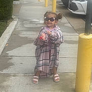 Auriella is registered to the contest to win money with this photo: child, girl, sunglasses, sidewalk, plaid_shirt, sandals, yellow_bollard, parking_lot, cars, smile, playful, pigtails, outdoor, concrete, street, wet_surface, person, clothing, accessory, urban