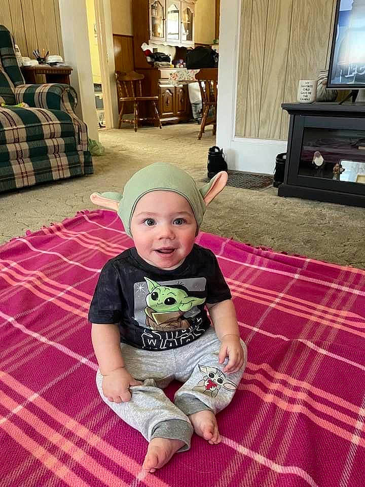Easton joined the competition — help win amazing prizes! baby, baby_toddler_clothing, blurred, carpet, chest_of_drawers, child, couch, floor, flooring, hardwood, headwear, home_appliance, lamp, living_room, pattern, person, room, sleeve, smile, t_shirt