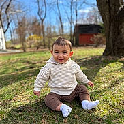 Jaxon is registered to the contest to win money with this photo: baby, child, smiling, grass, outdoor, hoodie, pants, socks, sunlight, tree, nature, happy, portrait, sitting, seasonal, daylight, casual_clothing, background_blur, yard, infant