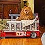 dog, pomeranian, toy_bed, fire_truck_design, blanket, quilt, wooden_floor, indoor, furniture, cabinet, vase, pet, cozy, cute, small_dog, fur, animal, home, living_room, decor