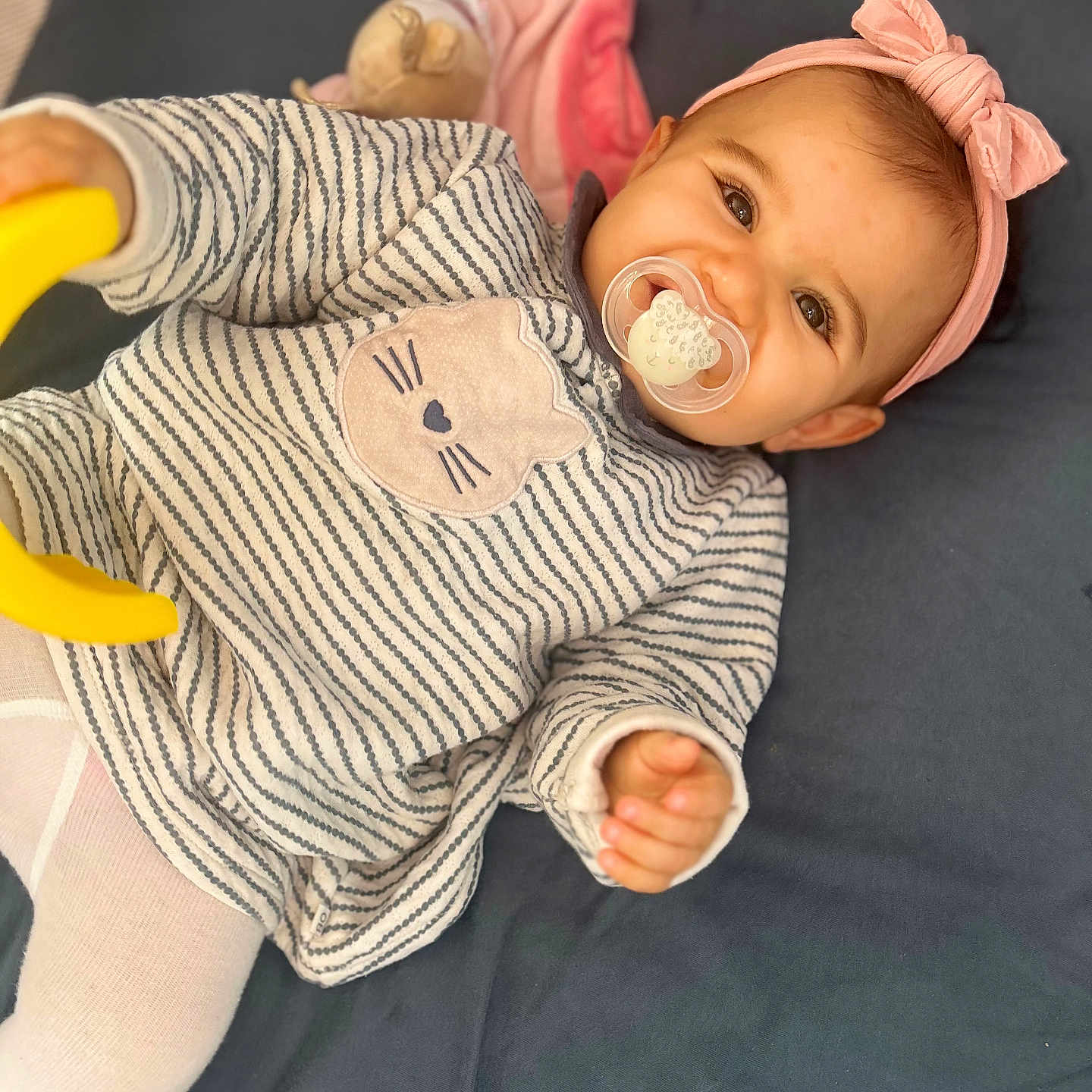 Almà participe au concours pour gagner de l'argent avec cette photo : baby, blanket, cat_design, child, closeup, cute, face, hand, headband, indoor, infant, lying_down, pacifier, person, pink, smile, soft_toy, striped_clothing, tights, toy