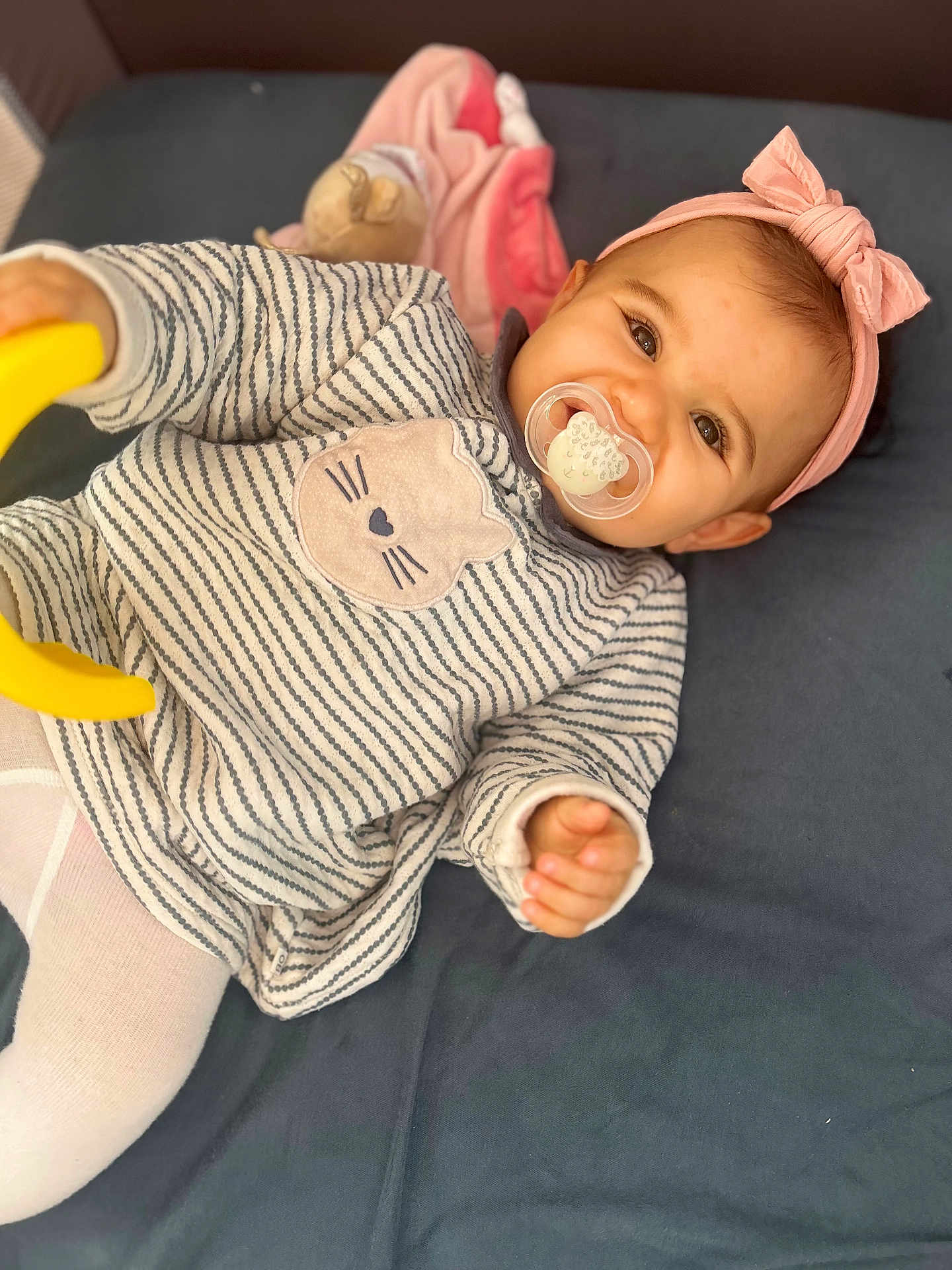 Almà participe au concours pour gagner de l'argent avec cette photo : baby, child, pacifier, headband, pink, toy, striped_clothing, cat_design, tights, smile, face, hand, lying_down, infant, cute, indoor, soft_toy, blanket, person, closeup