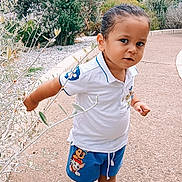 Abraham participe au concours pour gagner de l'argent avec cette photo : toddler, child, boy, outdoor, path, greenery, bushes, plants, white_shirt, blue_shorts, sandals, cartoon_characters, curious, standing, nature, daylight, casual_clothing, short_hair, expression, pavement