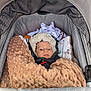baby, blanket, stroller, hood, face, child, cushion, clothing, fabric, soft_texture, indoor, person, infant, wrapped, warm, comfort, portrait, seated, cute, resting