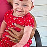 adult, arms, baby, being_held, bow, chair, child, fashion, happy, headband, infant, outdoor, polka_dots, porch, portrait, red_outfit, sitting, smiling, sparkly, wooden_wall