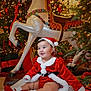 Madisson is registered to the contest to win money with this photo: baby, child, christmas, holiday, festive, santa_outfit, red_clothing, blanket, carousel_horse, decorations, christmas_tree, lights, smiling, indoor, cute, festive_shoes, holiday_season, cheerful, portrait, celebration