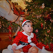 Madisson is registered to the contest to win money with this photo: baby, child, christmas, holiday, festive, tree, ornaments, lights, santa_claus, costume, red_shoes, blanket, carousel_horse, indoor, decorations, cute, smiling, celebration, holiday_season, portrait