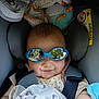 baby, blanket, blue, car_seat, child, clothing, comfort, cute, face, head, indoor, infant, reflection, safety, seatbelt, smile, soft_texture, sunglasses, toy, yellow